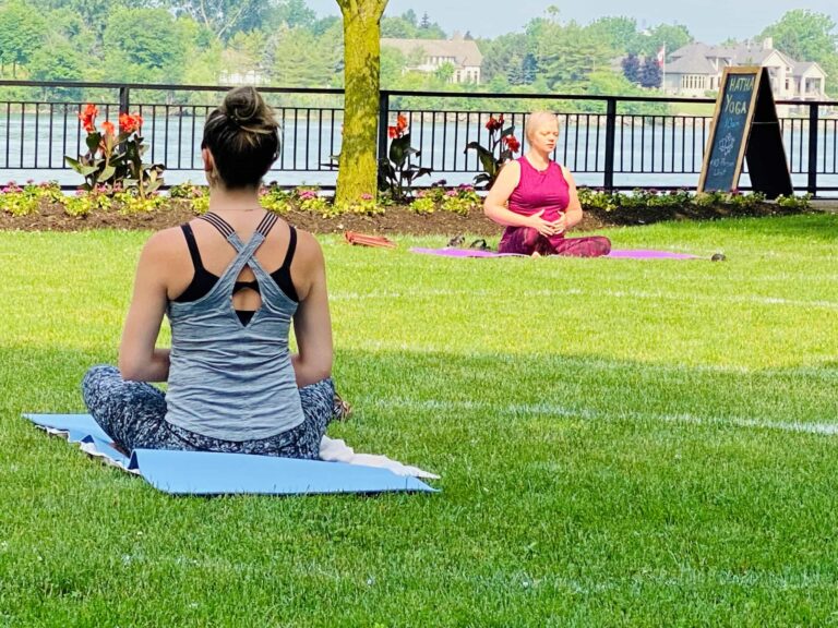 <p>Two women doing Hatha Yoga in the park by the water.</p>