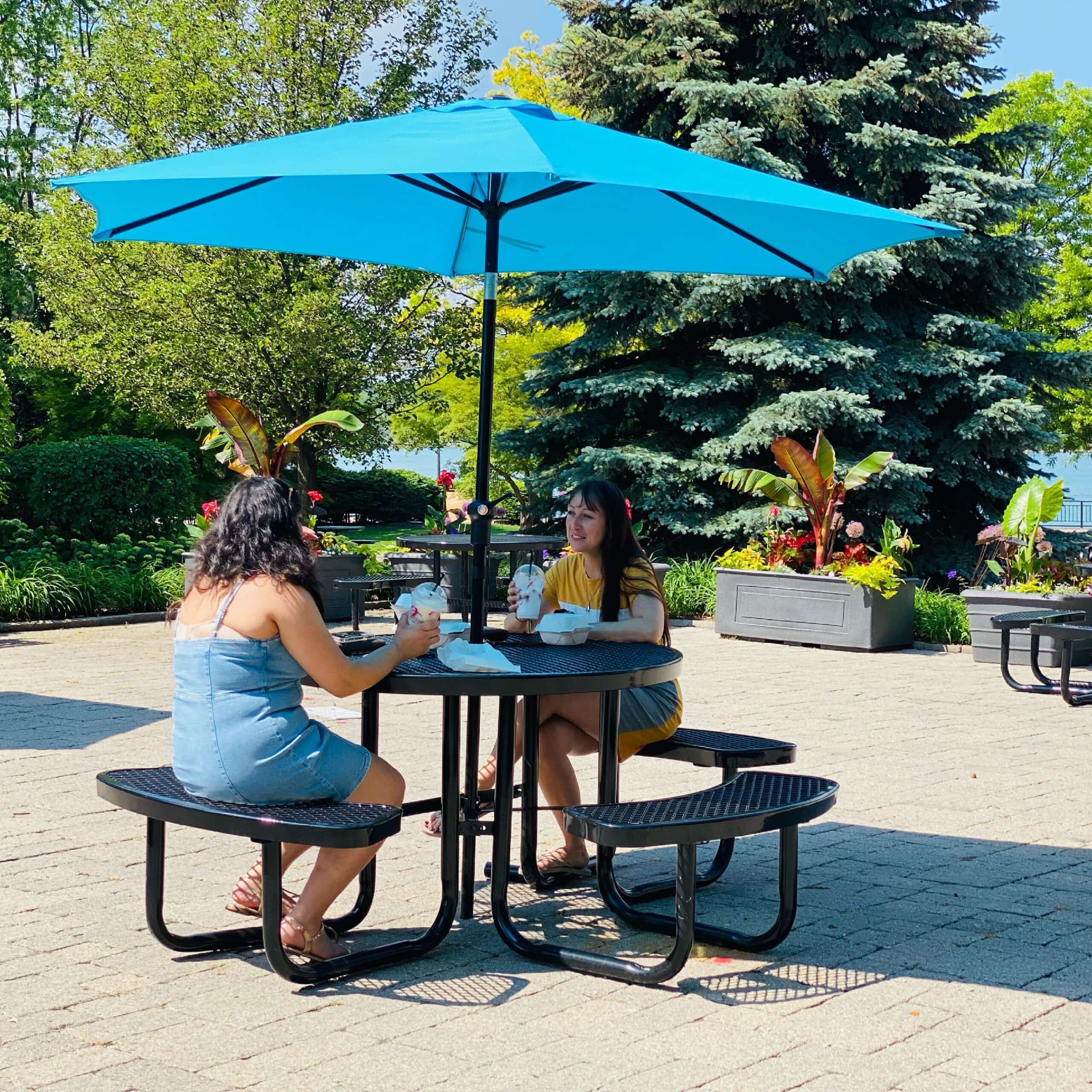 Two friends sit on a park bench and talk with milkshakes in hand.
