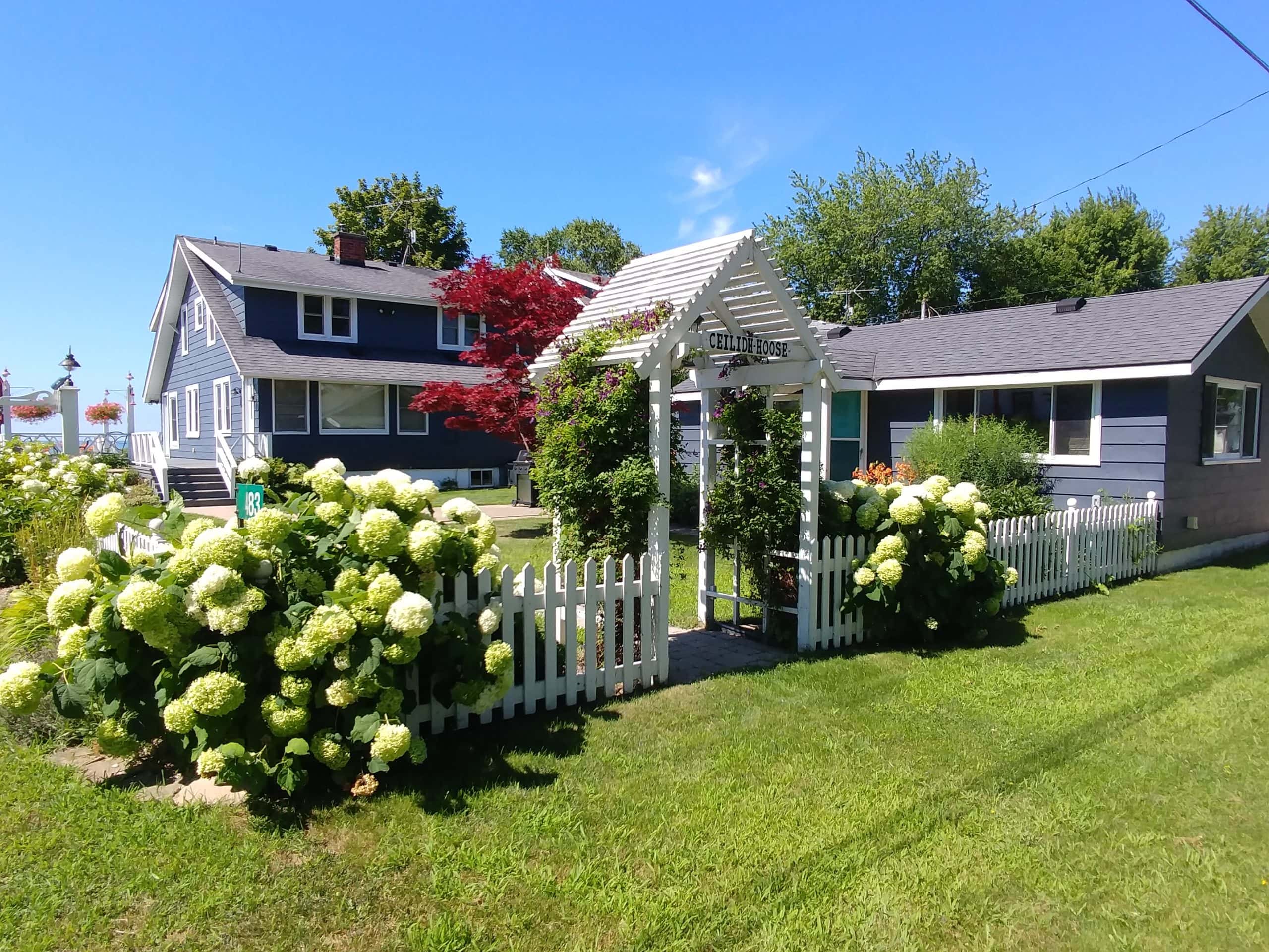 A blue home with beautiful gardens and a white picket fence along the water.