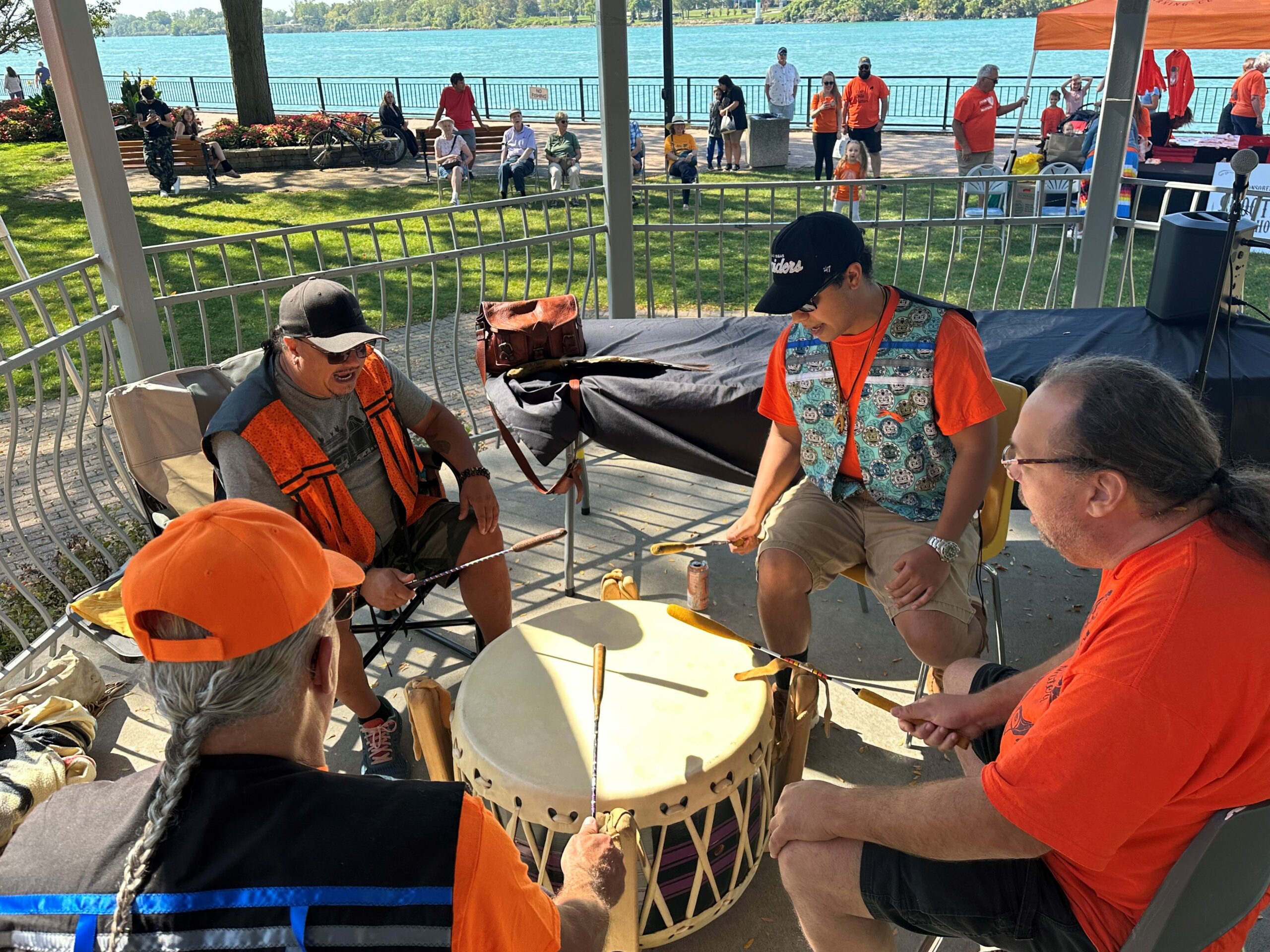 Four people drumming in a gazebo wearing orange during Truth and Reconciliation Gathering in Amherstburg