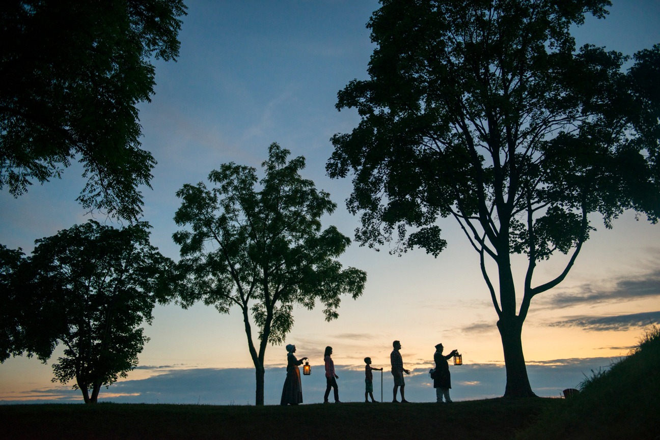 Line of people holding lanterns outside at sunset