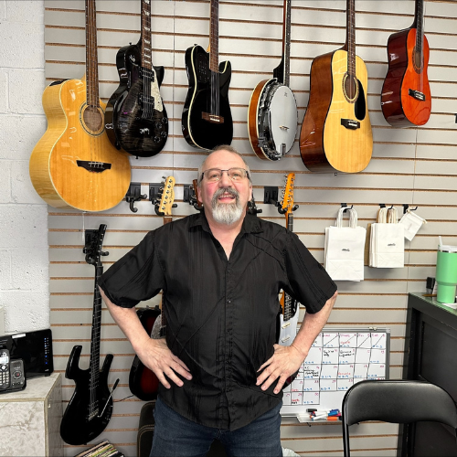 Denis Bastarache standing in front of a wall that has guitars on it
