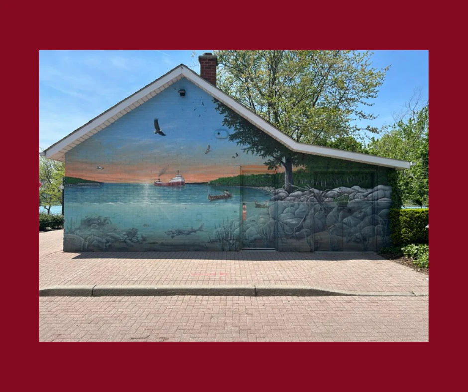A mural painted on a building featuring the waterway, a shoreline and a freighter ship
